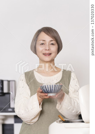 A senior woman pouring freshly cooked rice from a rice cooker into a bowl in the kitchen 137020330