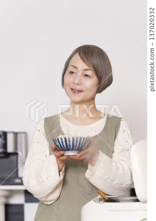 一位老婦人正在廚房裡把剛煮好的飯從電鍋裡倒進碗裡。 137020332