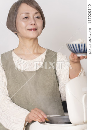 A senior woman pouring freshly cooked rice from a rice cooker into a bowl in the kitchen A senior woman pouring freshly cooked rice from a rice cooker into a bowl in the kitchen 137020340