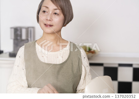 一位老婦人正在廚房裡把剛煮好的飯從電鍋裡倒進碗裡。 137020352