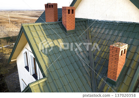 Green metal shingled house roof with attic plastic window and brick chimney. Green metal shingled house roof with attic plastic window and brick chimney. 137020358