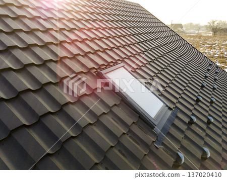 Close-up of new attic plastic window installed in shingled house roof. Professionally done building and construction work, roofing and installation concept. Close-up of new attic plastic window installed in shingled house roof. Professionally done building and construction work, roofing and installation concept. 137020410