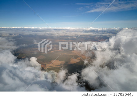 Aerial view from airplane window at high altitude of earth covered with white puffy cumulus clouds Aerial view from airplane window at high altitude of earth covered with white puffy cumulus clouds 137020443