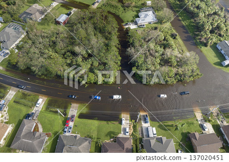 Flooded American street with moving vehicles and surrounded with water houses in Florida residential area. Consequences of hurricane natural disaster Flooded American street with moving vehicles and surrounded with water houses in Florida residential area. Consequences of hurricane natural disaster 137020451