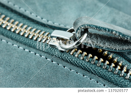 Detailed view of a silver metal zipper slider on textured blue suede leather fabric material 137020577
