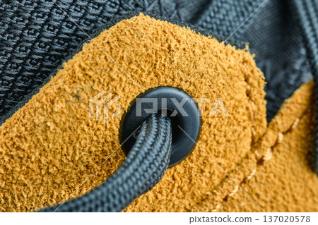 Macro shot of a black shoelace passing through a plastic eyelet on tan suede leather footwear 137020578