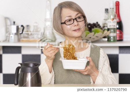 廚房裡，一位老婦人正往杯麵倒熱水。 137020790