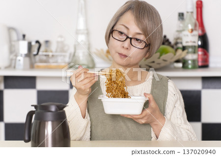 廚房裡，一位老婦人正往杯麵倒熱水。 137020940