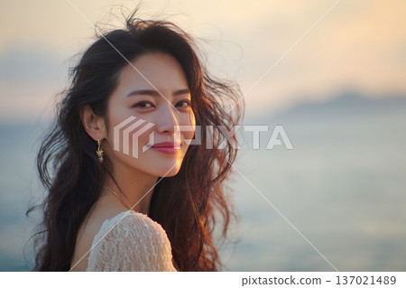 一張成年女性在海風中微笑的肖像照，她的肌膚在自然光下閃閃發光，散發著自由的氣息（橫幅照片） 137021489