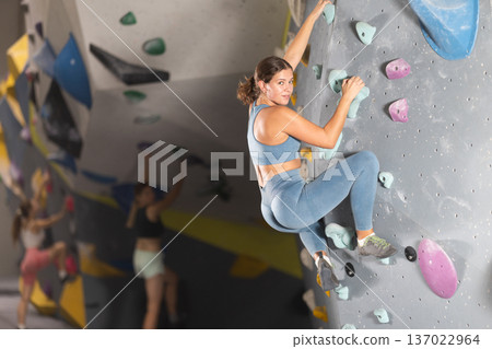 Girl in sportswear practicing rock climbing on climbing wall 137022964