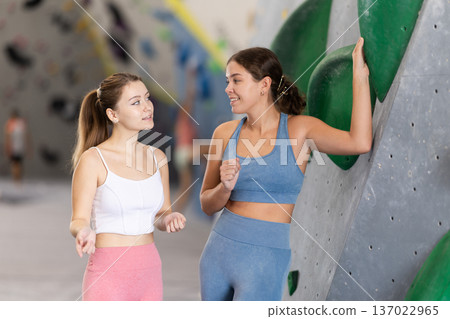 Female athletes communicate during break between workouts, gym climbing wall sport center 137022965