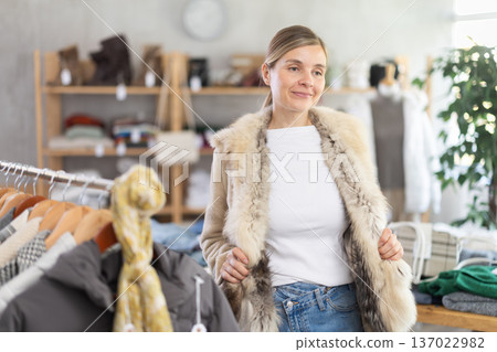 Woman try on fur jacket in front of mirror Woman try on fur jacket in front of mirror 137022982