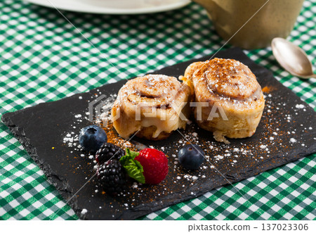 Tasty cinnamon rolls with fresh berries and powdered sugar at plate Tasty cinnamon rolls with fresh berries and powdered sugar at plate 137023306