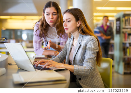 Two female students studying in library with books and laptop Two female students studying in library with books and laptop 137023339