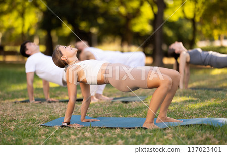 Girl performing Reverse Tabletop Pose during group yoga session in park 137023401