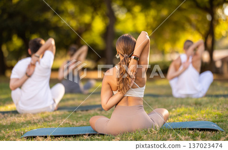Yoga lesson visitors with coach perform Paschima Namaskarasana in park 137023474