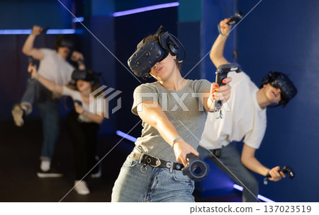 Young woman in VR glasses playing virtual game with handheld controllers Young woman in VR glasses playing virtual game with handheld controllers 137023519