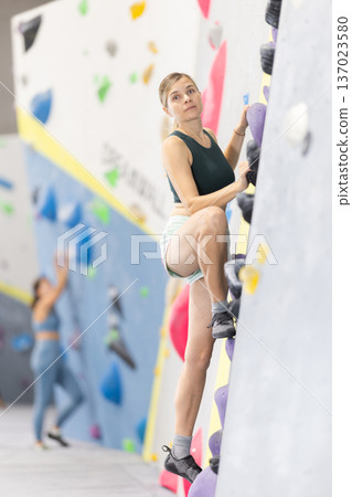 Woman climbs artificial wall bouldering, working out in gym Woman climbs artificial wall bouldering, working out in gym 137023580