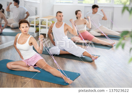 Young men and women doing arm workout with band sitting one leg extended 137023622
