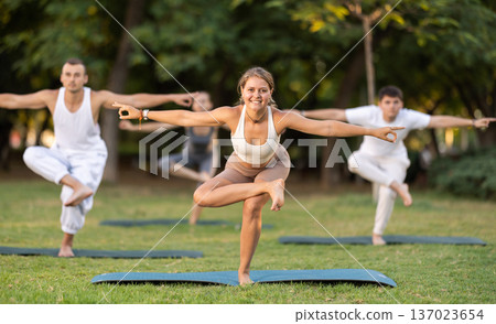 Girl doing Eka Pada Utkatasana at group yoga session in park 137023654