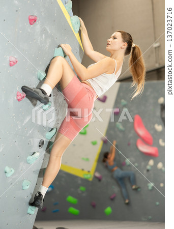 Girl climbs artificial wall bouldering, working out in gym Girl climbs artificial wall bouldering, working out in gym 137023716