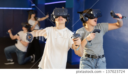 Young couple with handheld controllers and VR glasses playing game Young couple with handheld controllers and VR glasses playing game 137023724