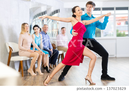 Brunette in red and young man enjoying tango in dance studio 137023829