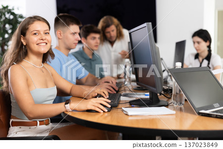 Among students of computer academy programmers, young girl is sitting and smiling, looking away Among students of computer academy programmers, young girl is sitting and smiling, looking away 137023849