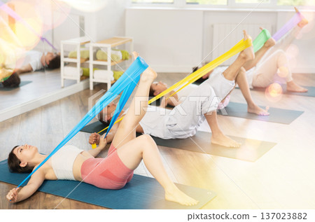 Young men and women practicing leg stretching with band lying back 137023882
