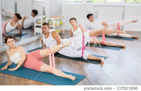 Young men and women practicing leg lift with band on knees lying on the side 137023890