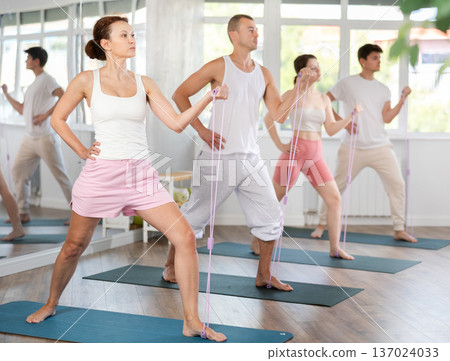 Sports focused young woman training with resistance band with group, strong biceps or abs muscles in gym health center Sports focused young woman training with resistance band with group, strong biceps or abs muscles in gym health center 137024033