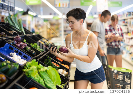 Latin american young female shopper choosing eggplants in store 137024126