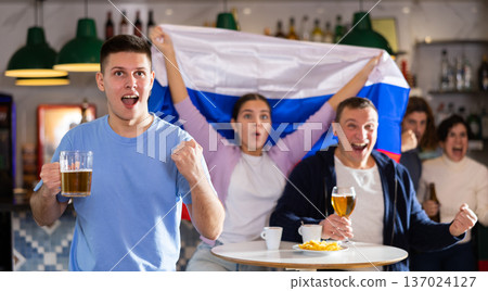Company of joyful supporters waving flag of Russia and celebrating victory of football team in sports bar 137024127