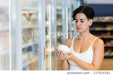 Interested Hispanic woman choosing dairy products on refrigerated shelves in shop Interested Hispanic woman choosing dairy products on refrigerated shelves in shop 137024162