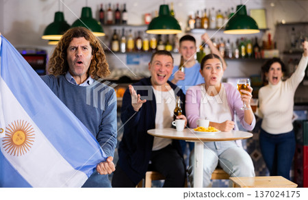 Group of excited friends holding flag of Argentina and supporting favorite game and drinking beer in bar Group of excited friends holding flag of Argentina and supporting favorite game and drinking beer in bar 137024175