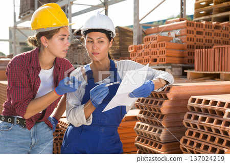 Women in hardhats discussing in outdoor warehouse Women in hardhats discussing in outdoor warehouse 137024219