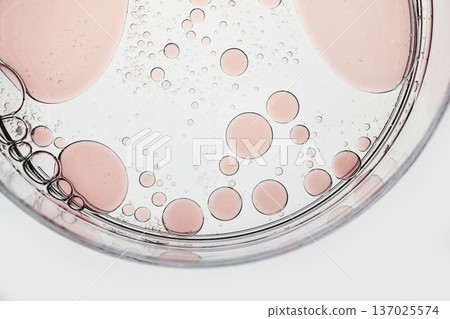 Pink liquid droplets and bubbles suspended in clear fluid within petri dish Pink liquid droplets and bubbles suspended in clear fluid within petri dish 137025574
