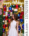 Woman in white dress posing at colorful holiday jewel wall backdrop 137025598