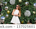 Woman in white dress posing by decorated Christmas tree outdoors 137025601