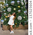 Woman in white dress posing at decorated Christmas tree outdoors 137025604