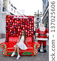 Woman sitting on red Santa sofa with ornament wall Christmas display outdoors 137025606