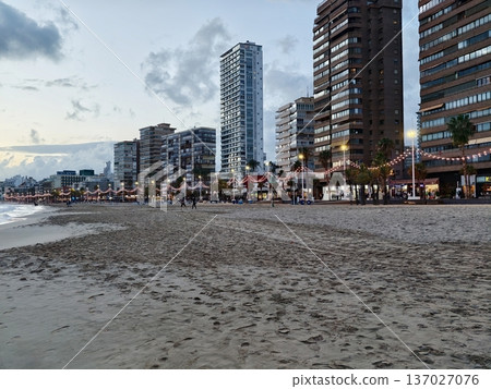 Sunset beach with lights, Serene night at coastal boardwalk with illuminated vendors and strollers Sunset beach with lights, Serene night at coastal boardwalk with illuminated vendors and strollers 137027076
