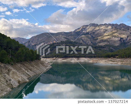 Peaceful landscape with reflective mountain lake, Calm waters among jagged mountains under cloudy sky 137027214
