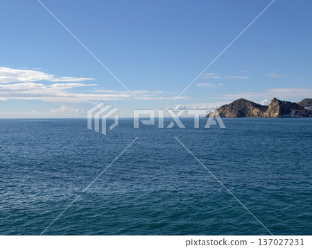 Tranquil waters with distant rocky promontory, Peaceful sea stretching to horizon with rocky headland 137027231