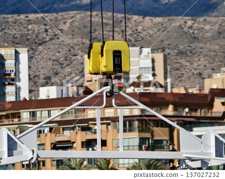 Crane over city, Construction crane perched over city rooftops with mountain backdrop and clear sky Crane over city, Construction crane perched over city rooftops with mountain backdrop and clear sky 137027232