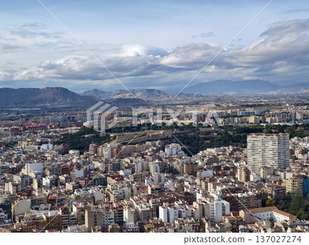Broad city horizon displaying mountain silhouettes and patchwork rooftops under gentle sunlight Broad city horizon displaying mountain silhouettes and patchwork rooftops under gentle sunlight 137027274