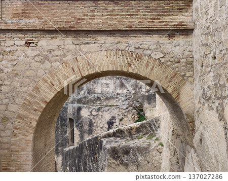 Ancient fort corridor with figure, Historic rampart corridor with distant figure and textured stones 137027286