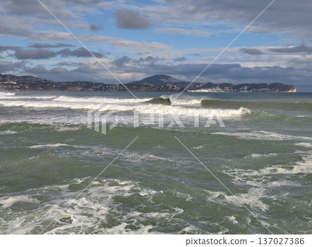 Immense marine vista showcasing moving waves and faraway mountains beneath layered sky formations Immense marine vista showcasing moving waves and faraway mountains beneath layered sky formations 137027386