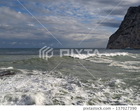Rough seaside cliffs and surf, Powerful waves crashing against steep rocky cliffs under cloudy weather Rough seaside cliffs and surf, Powerful waves crashing against steep rocky cliffs under cloudy weather 137027390