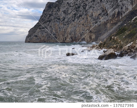 Rugged cliffs meet stormy waters, Dramatic shoreline featuring crashing waves and stormy clouds above Rugged cliffs meet stormy waters, Dramatic shoreline featuring crashing waves and stormy clouds above 137027398